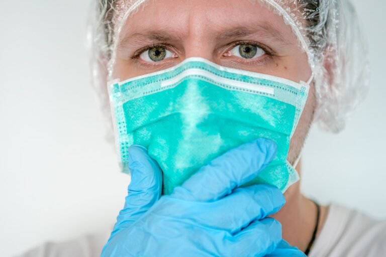 A men wears blue gloves, masks, and transparent hear cover