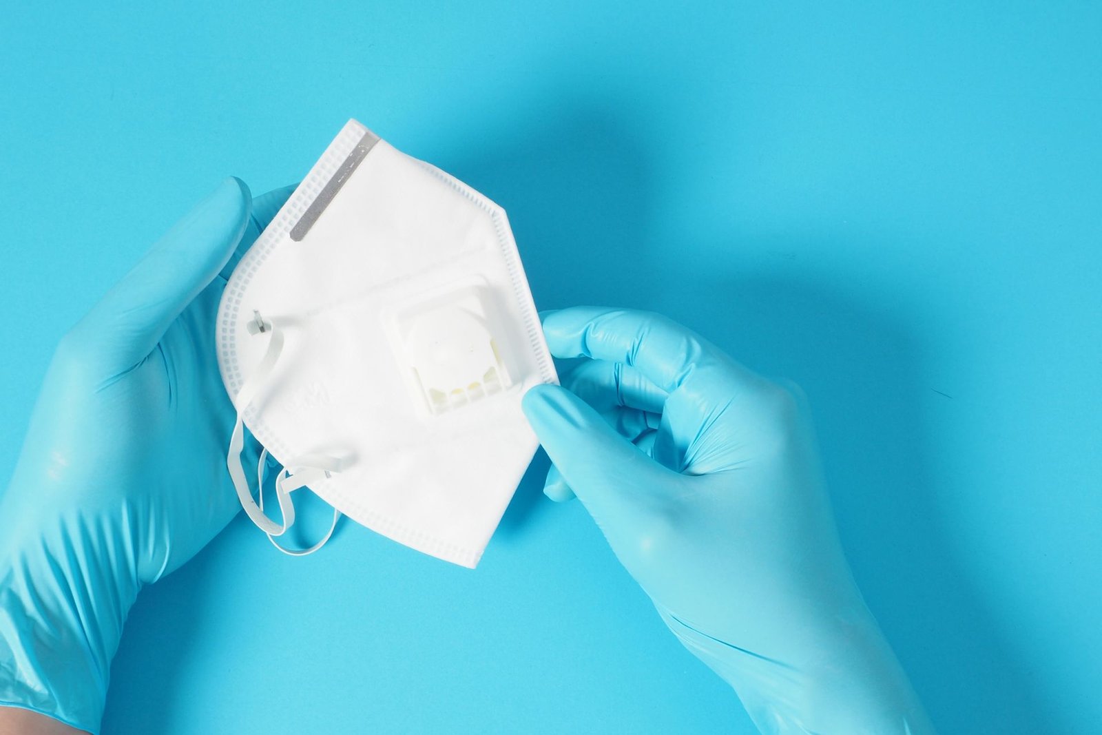 A person wear blue gloves hold N95 mask with blue background