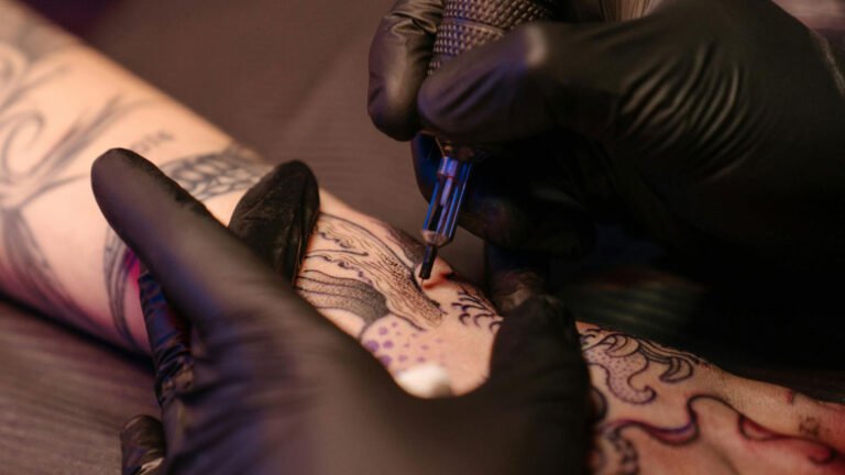 A tattoo artist adorned in sleek black gloves meticulously creates a masterpiece on a client's skin, embodying precision, professionalism, and artistry in a studio setting.