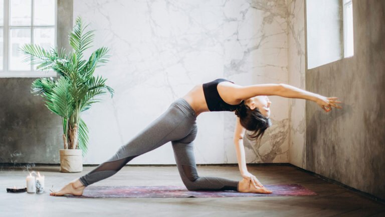 A woman in athletic attire gracefully performs a yoga pose, her arms outstretched and body balanced, embodying tranquility and mindfulness amidst a serene natural backdrop.